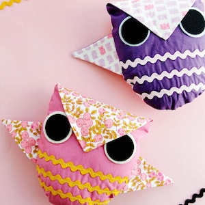 May include: Two handmade owl pillows with different fabric patterns. One owl is purple with white trim and the other is pink with yellow trim. Both owls have black felt eyes.
