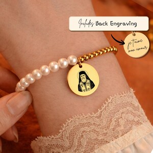 May include: A gold bracelet with a pearl and bead design. The bracelet has a round charm with a religious figure and the text "je t'aime mon amour" on a smaller charm. The text "Includes Back Engraving" is also visible.
