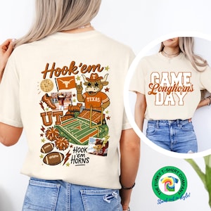 May include: Cream-colored t-shirt featuring a graphic with the text "Hook 'em" and "UT" with a Longhorn mascot, football field, and footballs. The shirt also has the text "Hook 'em Horns". Another shirt has the text "Game Longhorns Day".