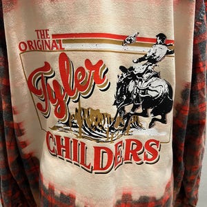 K&ouml;nnte beinhalten: Lang&auml;rmeliges rot-schwarz-wei&szlig; kariertes Hemd mit Grafik auf dem R&uuml;cken. Die Grafik zeigt die Worte "The Original Tyler Childers" mit einem Cowboy auf einem Pferd. Das Hemd hat einen gebleichten, verwaschenen Look.