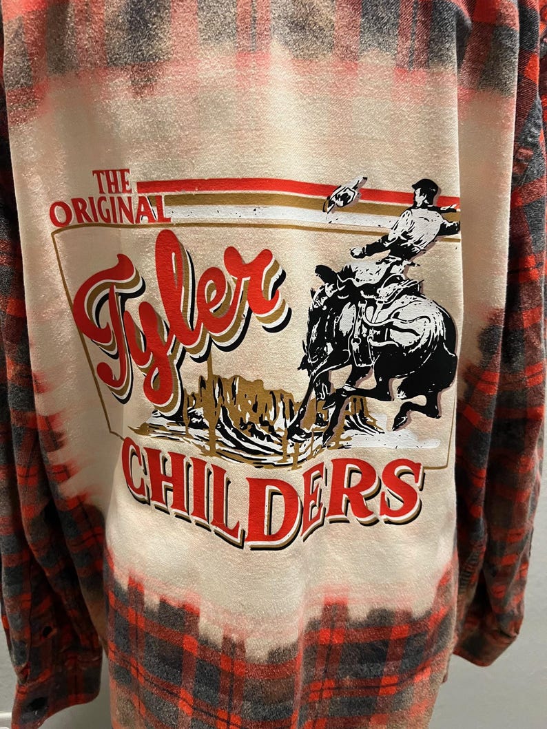 K&ouml;nnte beinhalten: Lang&auml;rmeliges rot-schwarz-wei&szlig; kariertes Hemd mit Grafik auf dem R&uuml;cken. Die Grafik zeigt die Worte "The Original Tyler Childers" mit einem Cowboy auf einem Pferd. Das Hemd hat einen gebleichten, verwaschenen Look.