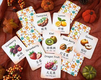 May include: A collection of fruit flashcards with watercolor illustrations and text in English and Chinese. The cards feature fruits like strawberries, kiwi, and dragon fruit, with a decorative pumpkin and leaf pattern on the back.