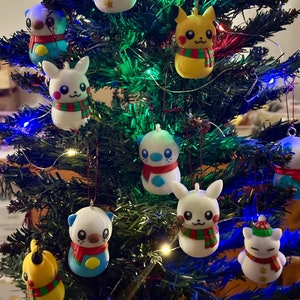 Peut inclure: Un sapin de Noël décoré de diverses décorations de personnages de dessins animés. Les décorations sont blanches, jaunes et bleues et présentent des personnages comme Pikachu et un lapin.