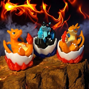 Może przedstawiać: Trzy małe plastikowe figurki postaci Pokemon, Charmandera, Squirtle'a i Bulbasaura, w ich formach jajowych. Figurki są odpowiednio pomarańczowe, niebieskie i zielone i stoją na drewnianej powierzchni.