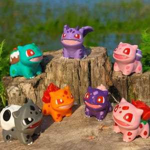 Op de afbeelding: Een set van zes handgeschilderde beeldjes van verschillende Pokémon-personages. De beeldjes zijn gemaakt van glad, kleurrijk plastic en zijn in verschillende speelse poses geposeerd. De personages zijn onder andere Bulbasaur, Charmander, Squirtle, Venusaur, Charmeleon en Blastoise.