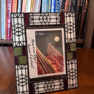 May include: A stained glass photo frame with a geometric design in white, black, burgundy, and green. The frame holds a photo with the text "Hello from Tokyo's Tsukimi Festival!" and the date "2025年9月".