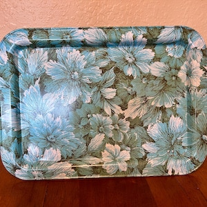 May include: A rectangular metal serving tray featuring a repeating floral pattern in shades of turquoise, light blue, and dark green. The tray has rounded corners and raised edges, with a glossy finish that highlights the detailed botanical illustrations.