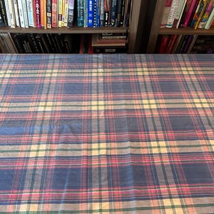 May include: A blue, pink, and yellow plaid fabric. The plaid pattern features intersecting lines of varying widths and colors, creating a classic design. The fabric is likely used for textiles or home decor.