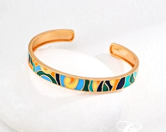 Puede incluir: Un brazalete de oro con un patrón geométrico colorido en tonos de azul, verde, amarillo y naranja.