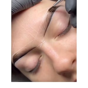 Könnte beinhalten: Nahaufnahme eines Gesichts, auf dem Henna auf die Augenbrauen aufgetragen wird. Der Text "HENNA BROWS SCHULUNG" wird am unteren Rand des Bildes angezeigt. Die Haut ist mit weißen Linien markiert, und die Augen der Person sind geschlossen.