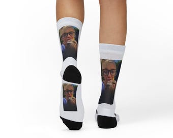 Op de afbeelding: Witte sokken met een zwarte hiel en teen, met een herhaalde afbeelding van een persoon met een bril. De sokken zijn zichtbaar vanaf de knieën, met de benen en voeten van de persoon in beeld.