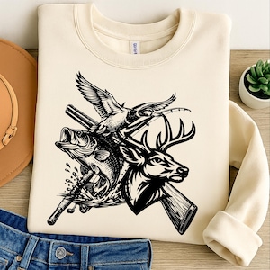 Pode incluir: Camisola creme com um gráfico a preto e branco de um veado, peixe e pato com uma cana de pesca e uma espingarda. O design tem um tema de caça e pesca.