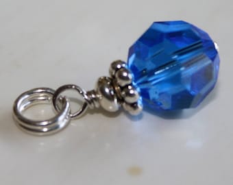 May include: A silver charm with a blue crystal bead and a silver jump ring.