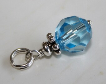 May include: A silver charm featuring a light blue crystal bead. The charm has a loop for attaching to a bracelet or necklace.
