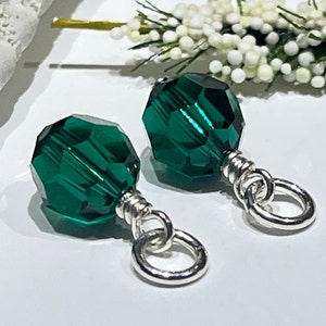 May include: A pair of emerald green crystal earrings with silver hoops. The earrings are made with faceted crystal beads and silver wire.