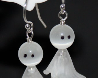 Op de afbeelding: Een paar witte, spookvormige oorbellen met zwarte ogen. De oorbellen zijn gemaakt van glas en hebben een delicaat, vrouwelijk ontwerp.