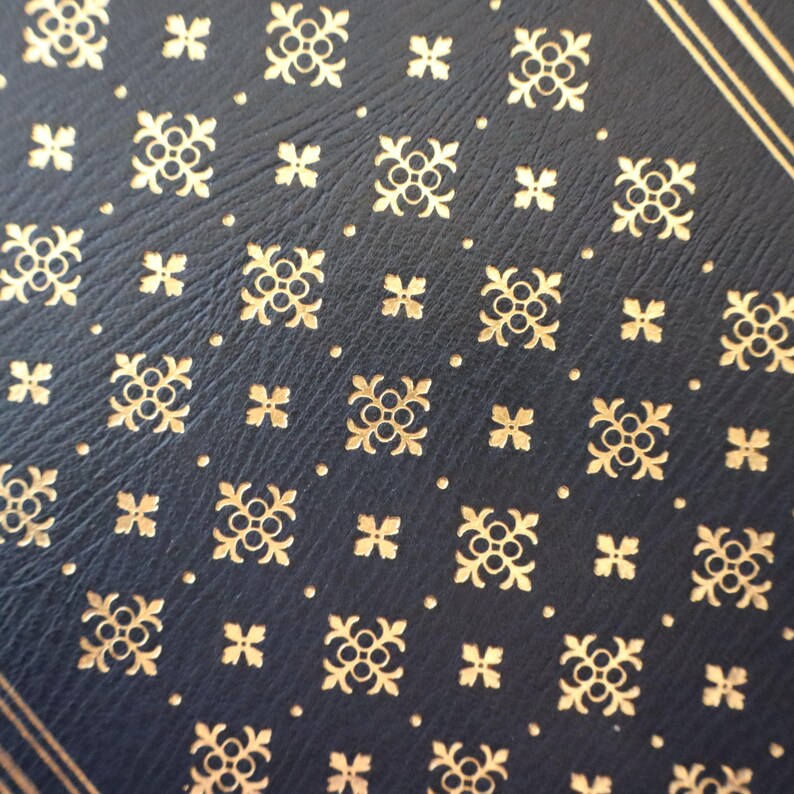 Puede incluir: Primer plano de una superficie de cuero azul oscuro con un patr&oacute;n repetitivo de dise&ntilde;os de tr&eacute;bol de cuatro hojas dorados en relieve.