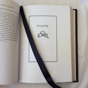 Puede incluir: Un libro abierto con un marcador de cinta negro. La p&aacute;gina est&aacute; titulada "Friendship" y presenta una simple ilustraci&oacute;n de dos gafas.
