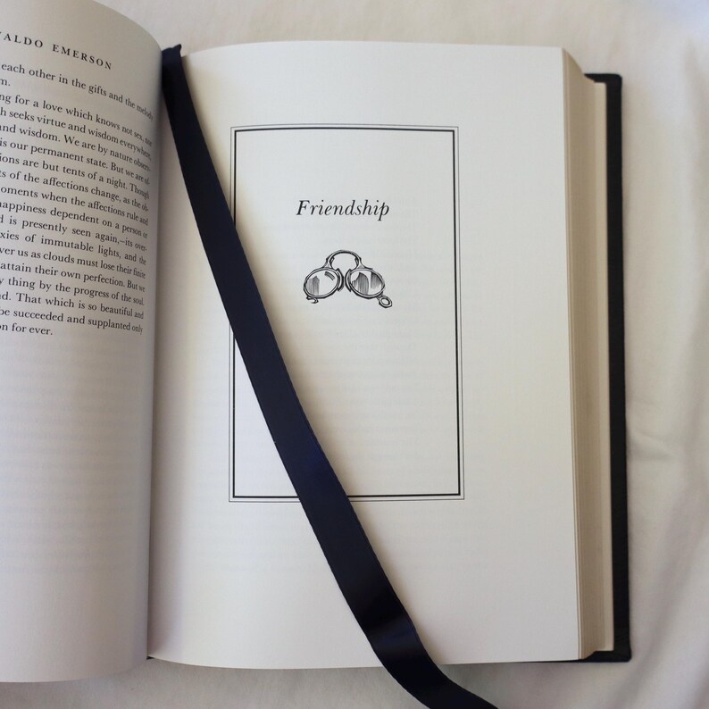 Puede incluir: Un libro abierto con un marcador de cinta negro. La p&aacute;gina est&aacute; titulada "Friendship" y presenta una simple ilustraci&oacute;n de dos gafas.