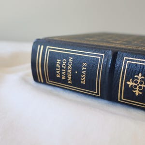 Puede incluir: Un libro encuadernado en cuero negro con letras doradas en el lomo. El t&iacute;tulo dice "Ralph Waldo Emerson Essays".