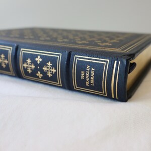 Puede incluir: Primer plano del lomo de un libro encuadernado en cuero negro con letras doradas que dicen "The Franklin Library".