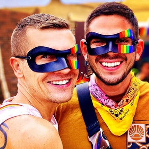May include: Two people wearing rainbow-colored eye masks. The person on the left is wearing a black eye mask with rainbow accents. The person on the right is wearing a black eye mask with rainbow stripes. The person on the right is wearing a yellow bandana with pink and white stripes and the text "Bumble" printed on it.