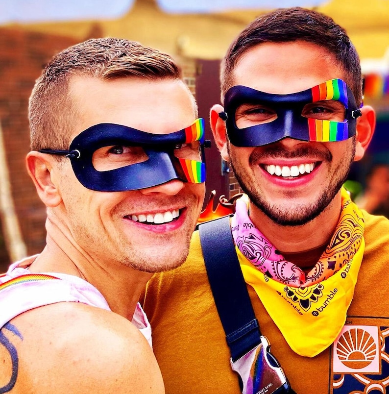 May include: Two people wearing rainbow-colored eye masks. The person on the left is wearing a black eye mask with rainbow accents. The person on the right is wearing a black eye mask with rainbow stripes. The person on the right is wearing a yellow bandana with pink and white stripes and the text "Bumble" printed on it.