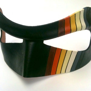 May include: A black leather mask with a rainbow stripe design. The mask has a large eye opening and a small opening for the nose.