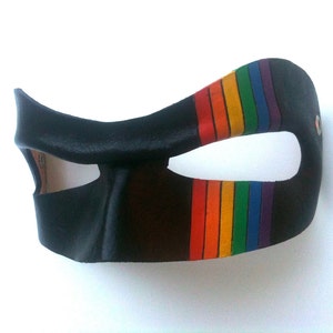 May include: A black leather mask with a rainbow stripe design. The mask has a single eye hole and is designed to cover the eyes and nose.