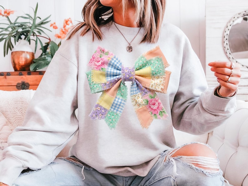 Pu&ograve; includere: Una felpa grigio chiaro con un grande design a fiocco patchwork colorato. L'arco incorpora motivi floreali, quadretti e colori pastello a tinta unita. L'arco &egrave; il punto focale della felpa, creando un look stravagante e artistico.