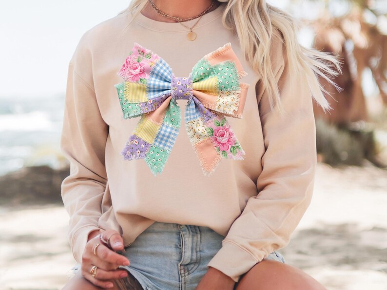 Pu&ograve; includere: Una felpa beige con un'applicazione a fiocco grande e colorata. Il fiocco &egrave; realizzato in tessuto patchwork nei colori pastello, tra cui fiori rosa, quadretti blu e quadrati gialli e verdi a tinta unita. Il fiocco &egrave; il punto focale del top casual.