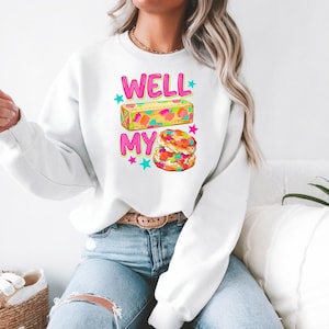 May include: A white long-sleeve crewneck sweatshirt featuring a graphic print with the text WELL MY in bright pink letters. The design includes a rectangular block of butter and two stacked biscuits, both decorated with colourful confetti sprinkles.