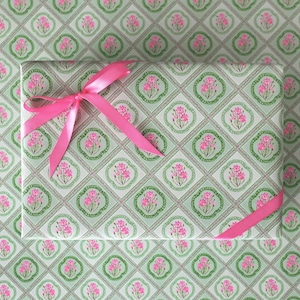 May include: A wrapped gift with a pink ribbon bow, set against a matching floral patterned wrapping paper background. The paper features a repeating design of pink flowers within green and white diamond shapes.