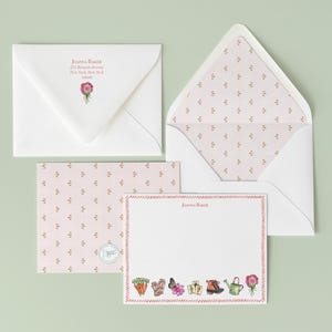May include: Stationery set featuring a white envelope with a floral design and the name "Joanna Baker". The set includes a matching envelope with a floral interior, a notecard, and a patterned card with a floral design.