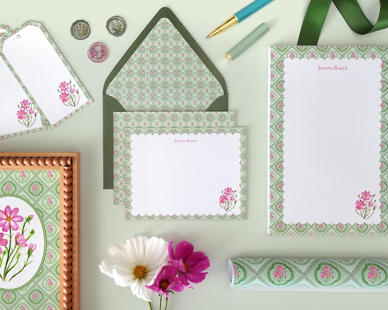 May include: Stationery set featuring a floral design with pink flowers and a green and white pattern. Includes notepaper, envelopes, tags, and a framed print. A pen and ribbon are also visible.