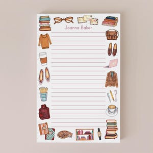 May include: A lined notepad with illustrations of books, eyeglasses, a sweater, coffee, shoes, and other items. The notepad has the name "Joanna Baker" at the top. The illustrations are in a watercolor style.