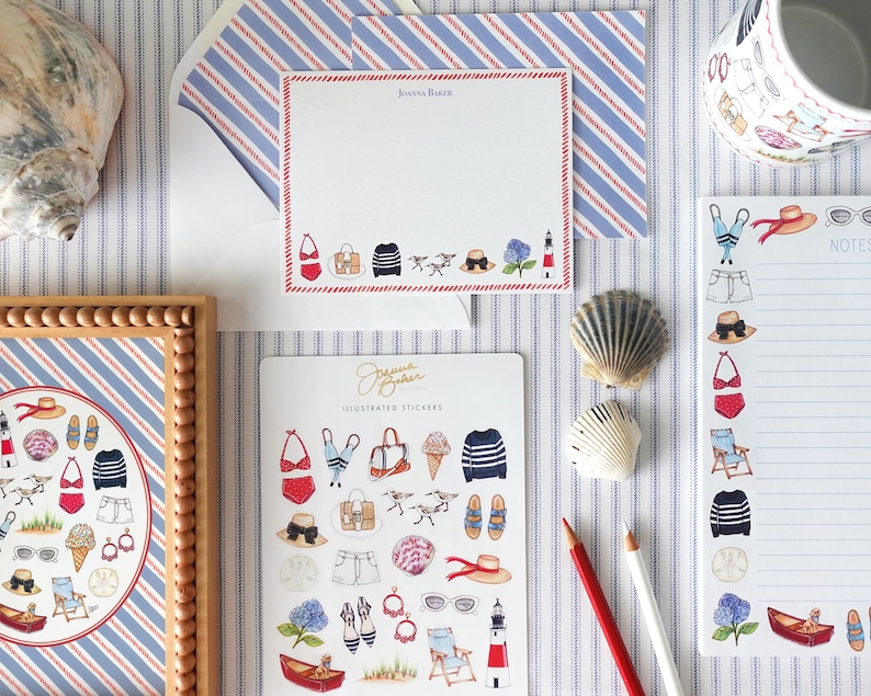 K&ouml;nnte beinhalten: Eine Auswahl an nautisch thematisierter Schreibwaren und Aufklebern. Das Bild zeigt einen gerahmten Druck, Notizbl&ouml;cke, Aufkleber und eine Tasse, alle mit Illustrationen von Strandartikeln wie Badeanz&uuml;gen, H&uuml;ten und Segelbooten. Die Farbpalette ist haupts&auml;chlich rot, wei&szlig; und blau.