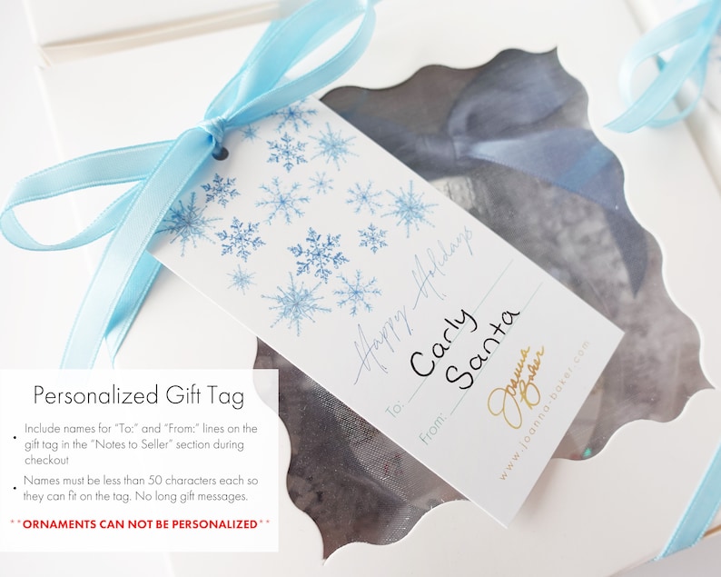 K&ouml;nnte beinhalten: Ein wei&szlig;es Geschenkanh&auml;nger mit einem blauen Schneeflockenmuster. Der Anh&auml;nger hat den Text "Happy Holidays" in Kursivschrift. Der Anh&auml;nger hat auch den Text "To: Carly Santa" in Kursivschrift. Der Anh&auml;nger hat den Text "From:" in Kursivschrift. Der Anh&auml;nger hat den Text "Joanna Baker" in Kursivschrift. Der Anh&auml;nger hat den Text "www.joanna-baker.com" in Kursivschrift.