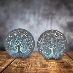 May include: Two round blue and white coasters with a tree of life design. The tree is surrounded by stars, moons, and other celestial symbols. The coasters are made of a cork-like material.