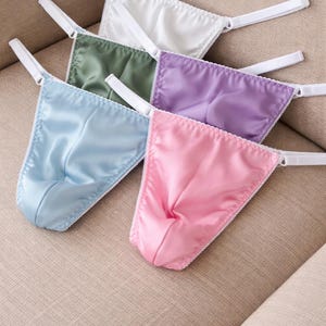 May include: A collection of satin thong underwear in various pastel colors: white, green, purple, light blue, and pink. Each thong features a delicate lace trim and white adjustable straps.