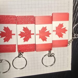 May include: Four red, white and red Canadian flag keyrings with silver key rings. The flags are printed on a textured surface.