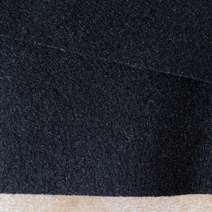 Puede incluir: Primer plano de una tela negra con una superficie texturizada. La tela es suave y tiene un aspecto ligeramente peludo.