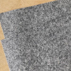 Puede incluir: Primer plano de dos piezas de tela de fieltro gris. La tela tiene una textura suave y peluda.