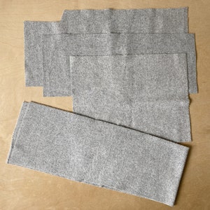 Puede incluir: Un conjunto de cinco piezas de tela de fieltro gris, cortadas en forma rectangular, dispuestas sobre una superficie marrón claro.