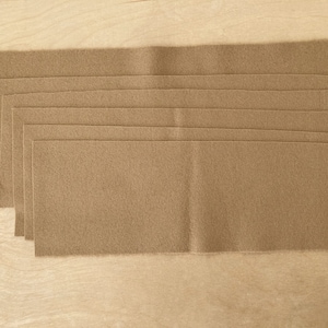 Puede incluir: Una pila de ocho hojas de fieltro marrón, cada una mide aproximadamente 30 cm por 46 cm.