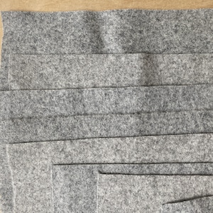 Puede incluir: Una pila de tiras de tela de fieltro gris. La tela es suave y tiene una superficie ligeramente texturizada.