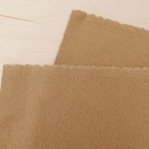 Puede incluir: Dos piezas de tela de fieltro marrón con una textura ligeramente rugosa. La tela está doblada, mostrando los bordes.