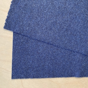 Puede incluir: Dos piezas de tela de fieltro azul oscuro dobladas una encima de la otra. La tela tiene una superficie ligeramente texturizada.