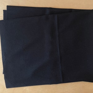 Puede incluir: Un trozo de tela negra doblado. La tela es lisa y tiene un ligero brillo.