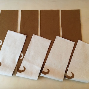 Puede incluir: Cinco tiras de tela, dos marrones y tres blancas, con un patrón geométrico. La tela está dispuesta en forma escalonada, con las tiras marrones encima de las tiras blancas.